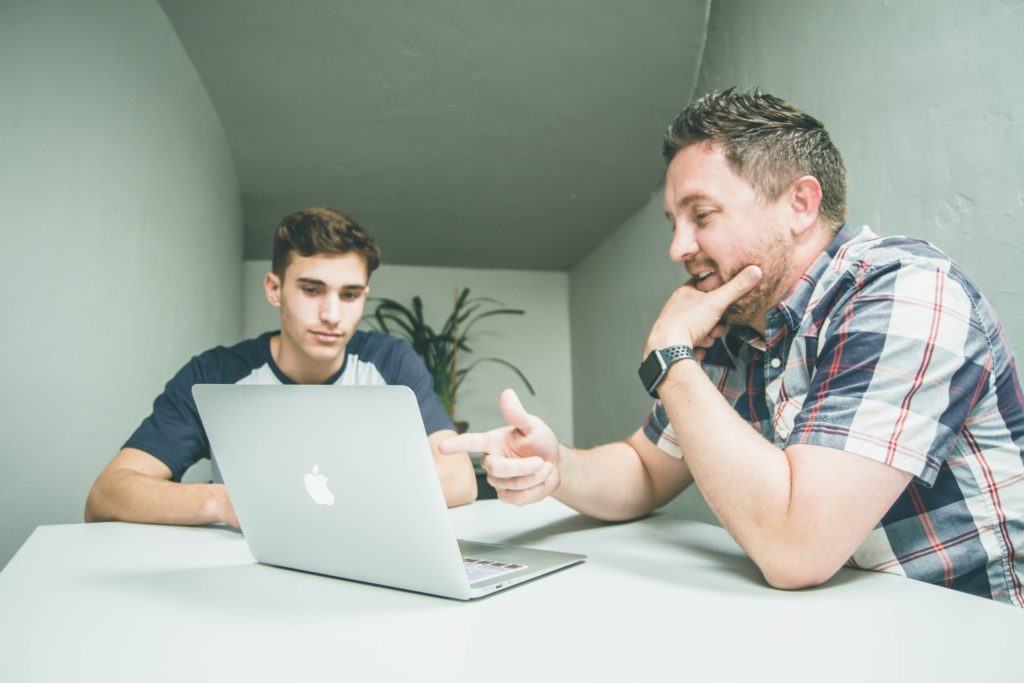 Two men sat at table looking at laptop, mentorship