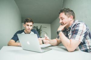 Two men sat at table looking at laptop, mentorship